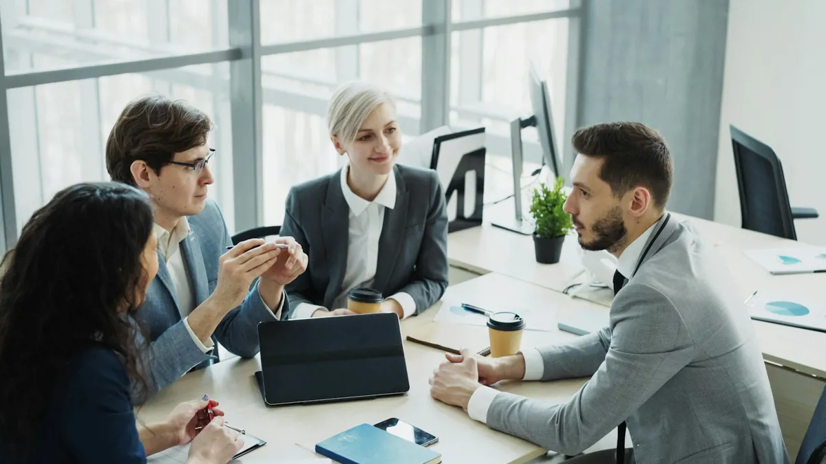 Vier Kolleginnen und Kollegen im Gespräch an einem Besprechungstisch in einem hellen Büro